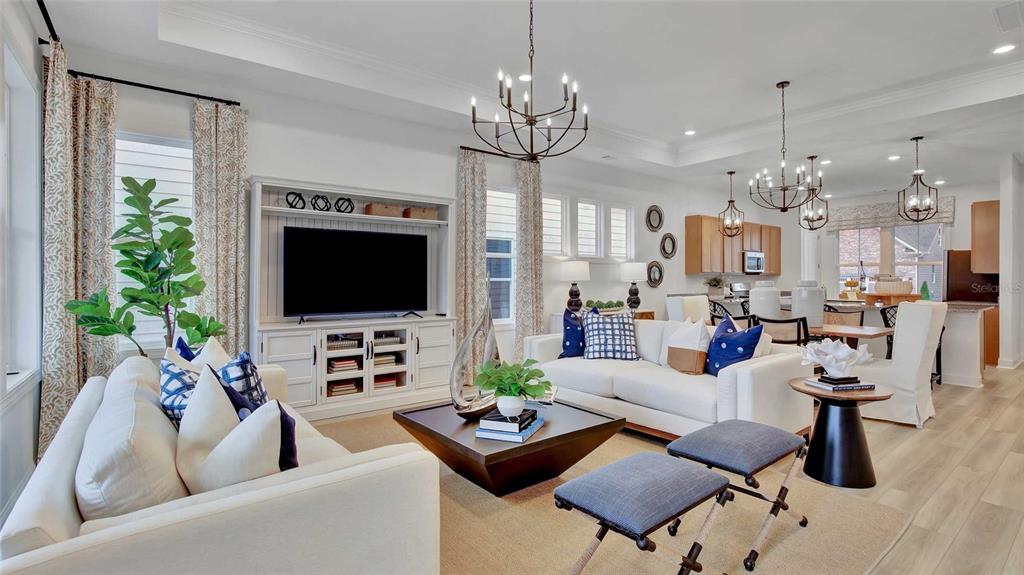 A bright, open-concept living room and kitchen featuring white cabinetry, chandeliers, and neutral furnishings — 1533 TREGAN AVENUE, DELAND, FL