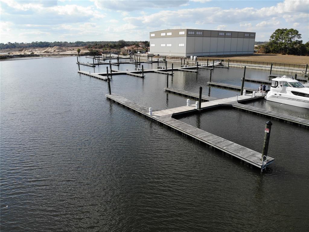 An aerial view shows a marina with multiple wooden boat slips and a large warehouse — 1 MARINA DEL PALMA UNIT B21, PALM COAST, FL