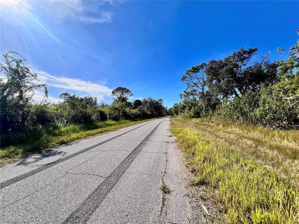A paved road with tire tracks stretches through a rural landscape with trees and grass — 12188 KILMER AVENUE, PORT CHARLOTTE, FL