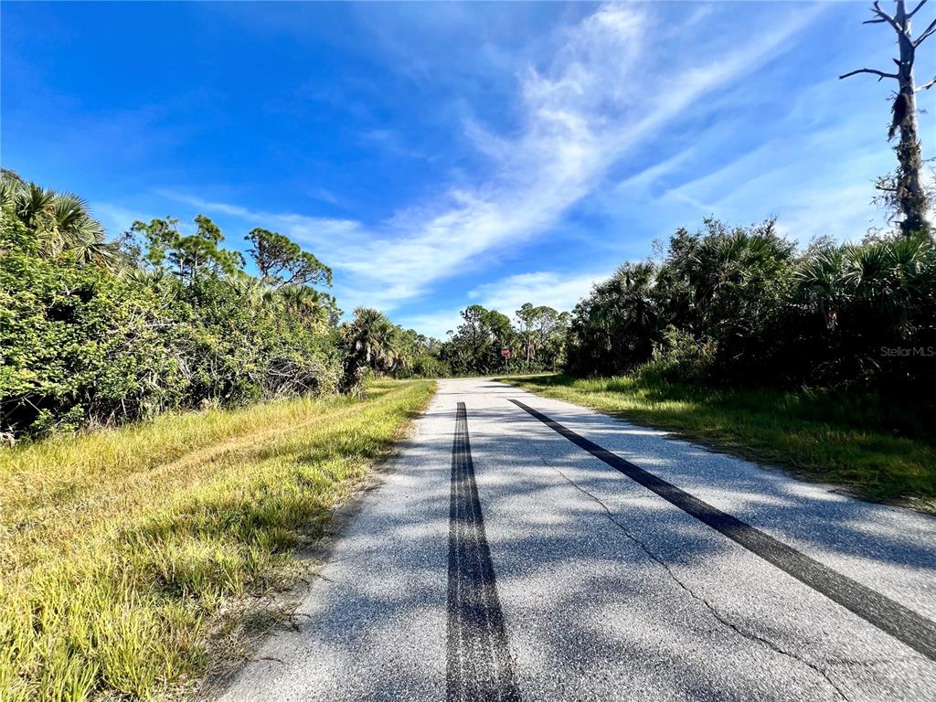 A paved road with tire tracks leads through a wooded area under a blue sky — 12188 KILMER AVENUE, PORT CHARLOTTE, FL