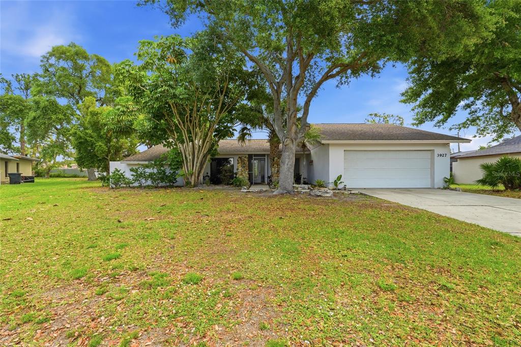 A single-story house with a white garage, a large front lawn, and mature trees — 3927 COUNTRY VIEW LANE, SARASOTA, FL