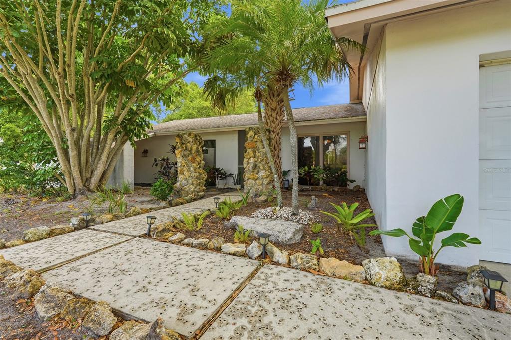 A concrete walkway leads to the entrance of a house with stone pillars and landscaping — 3927 COUNTRY VIEW LANE, SARASOTA, FL