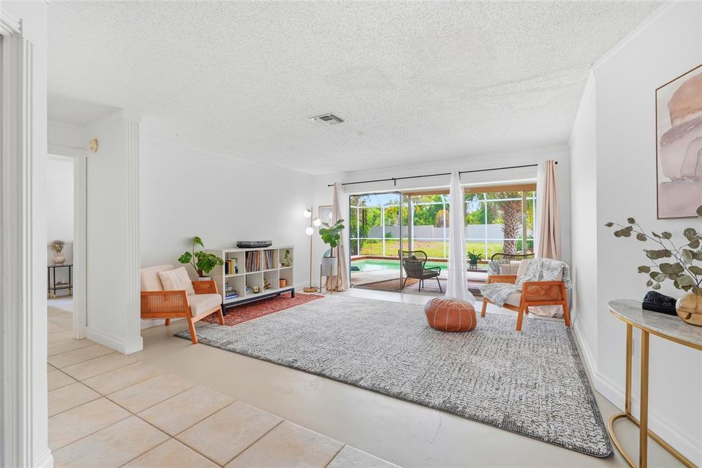 A bright living room features a large area rug, two armchairs, and sliding glass doors — 3927 COUNTRY VIEW LANE, SARASOTA, FL