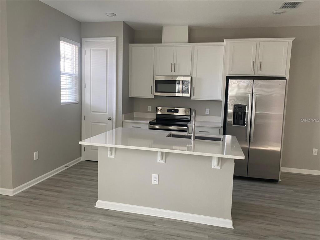 A kitchen features white cabinets, stainless steel appliances, a center island, and wood-look flooring — 1457 AXEL GRAESON AVENUE, KISSIMMEE, FL