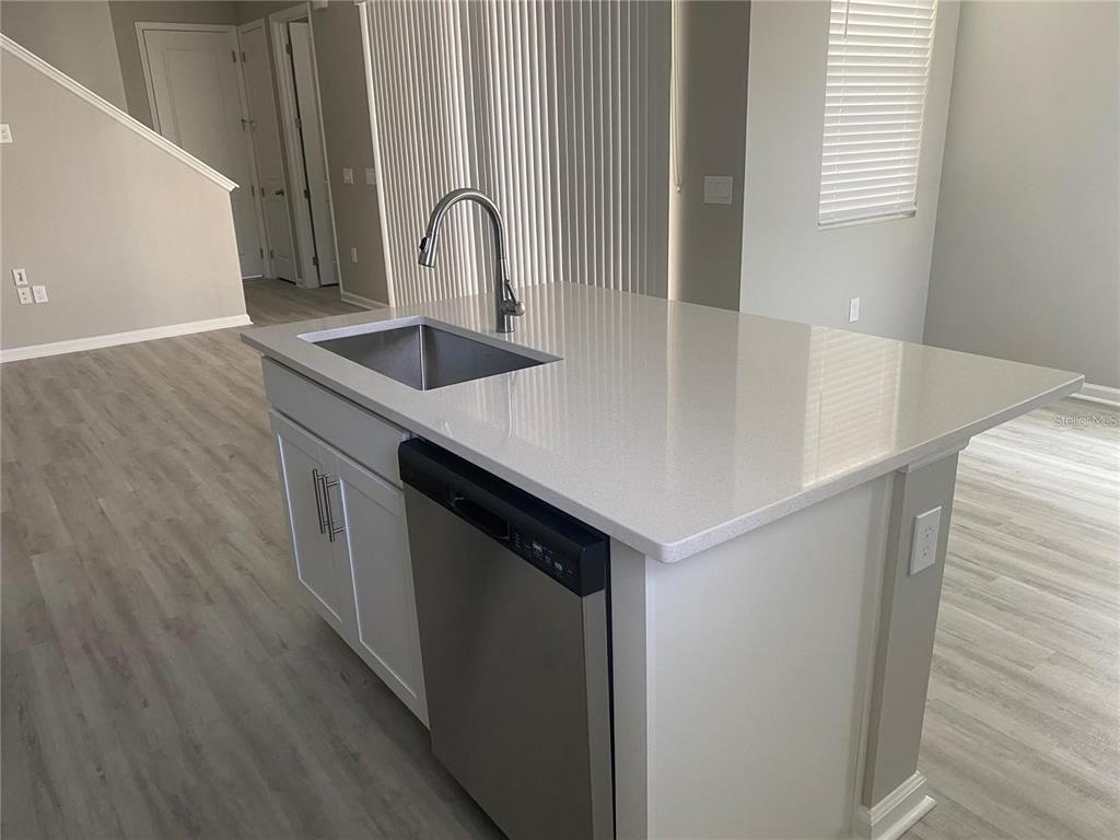 A kitchen island features a stainless steel sink, a dishwasher, and light-colored quartz countertops — 1457 AXEL GRAESON AVENUE, KISSIMMEE, FL