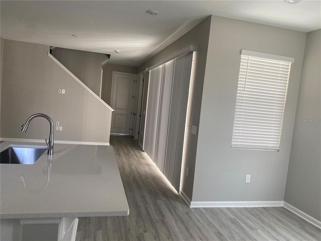 A kitchen island with a sink overlooks a hallway with stairs and sliding glass doors — 1457 AXEL GRAESON AVENUE, KISSIMMEE, FL