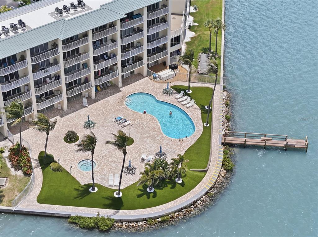 An aerial view of a waterfront apartment building with a pool, hot tub, and dock — 8800 BAY PINES BOULEVARD UNIT 216, ST PETERSBURG, FL