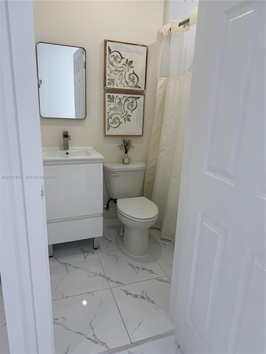A small bathroom features a white vanity, a toilet, and white marble-patterned floor tiles — HOMESTEAD, FL