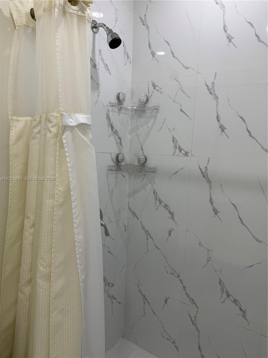 A shower stall features white marble-patterned wall tiles, a showerhead, and two clear corner shelves — HOMESTEAD, FL