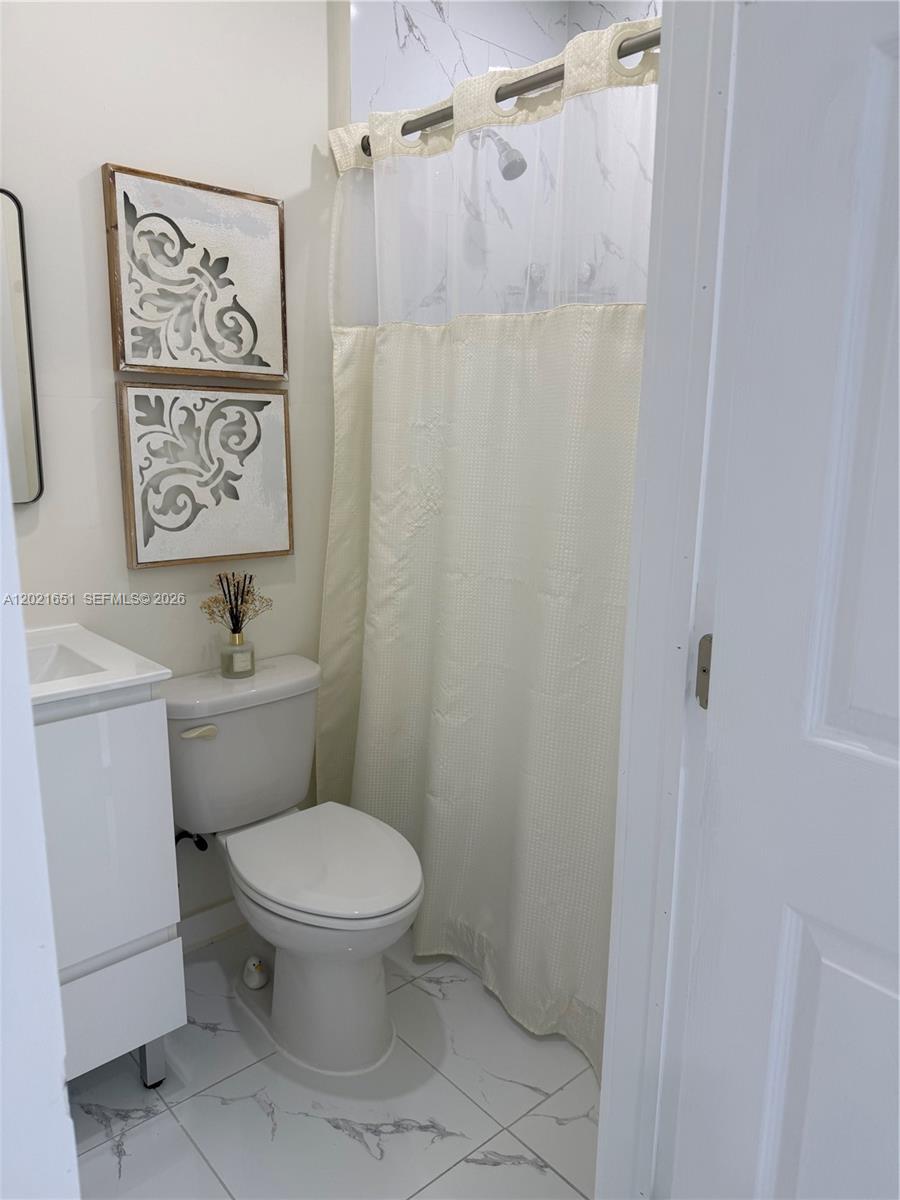 A small bathroom features a white vanity, a toilet, and a shower with a curtain — HOMESTEAD, FL