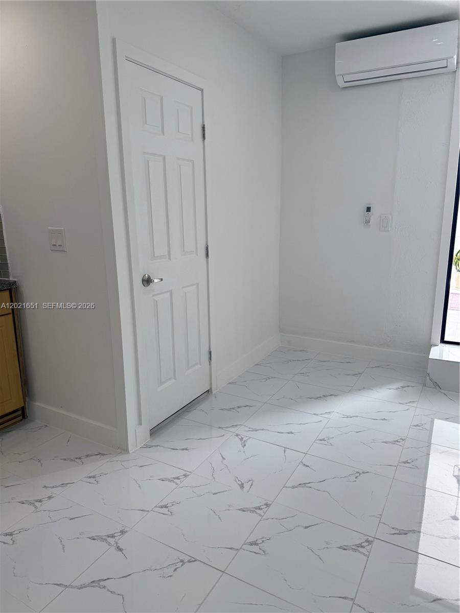 A room with white marble-patterned tile flooring, a white door, and a wall-mounted air conditioner — HOMESTEAD, FL