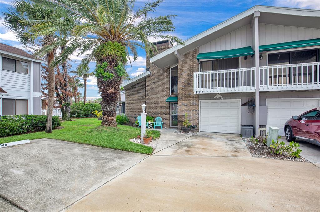 A two-story brick townhouse with a palm tree, a driveway, and a balcony — 113 LAGOON COURT, NEW SMYRNA BEACH, FL