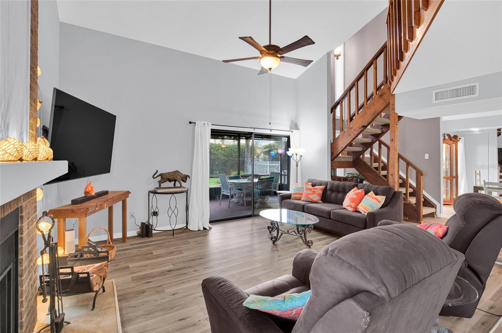 A living room features a fireplace, a staircase, wood-look flooring, and a sliding glass door — 113 LAGOON COURT, NEW SMYRNA BEACH, FL