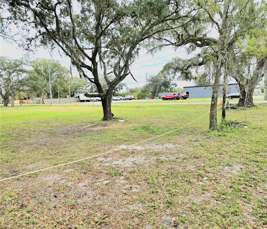 A grassy, tree-filled vacant lot features a rope boundary line stretching across the foreground — 3416 FLAT ROAD, LAKELAND, FL