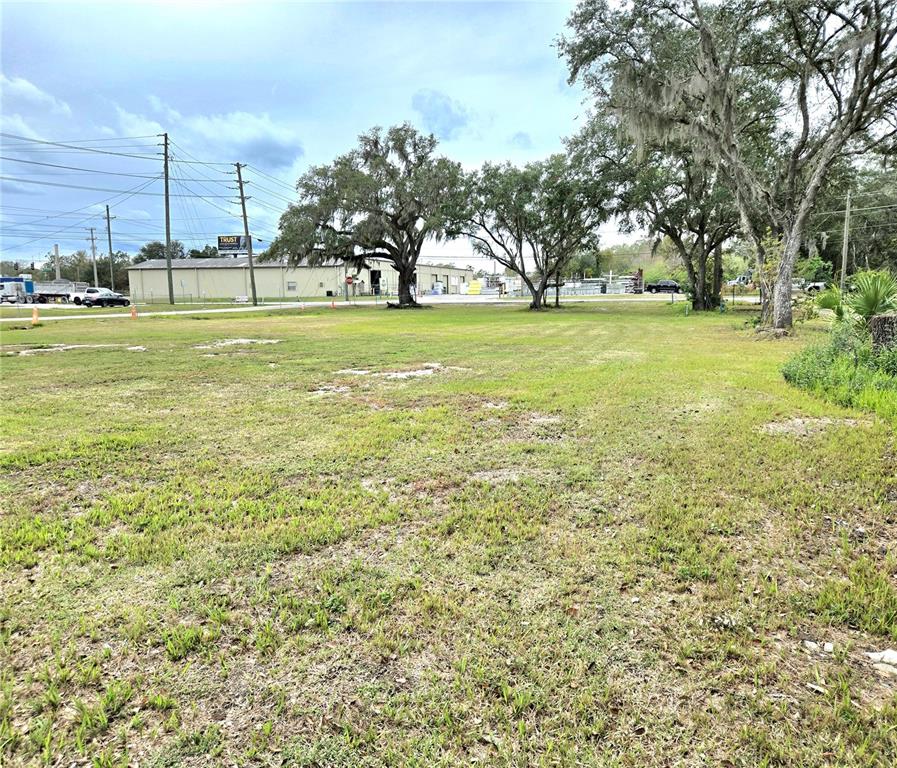 A large, grassy vacant lot features several mature trees under a cloudy sky — 3416 FLAT ROAD, LAKELAND, FL