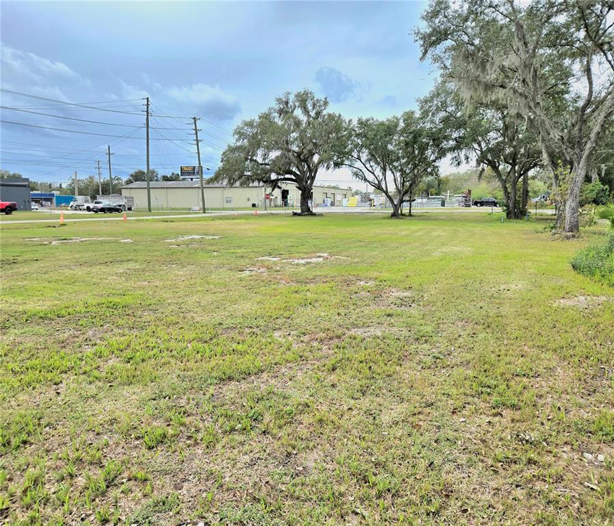 A wide, grassy vacant lot features several large oak trees under a cloudy sky — 3416 FLAT ROAD, LAKELAND, FL