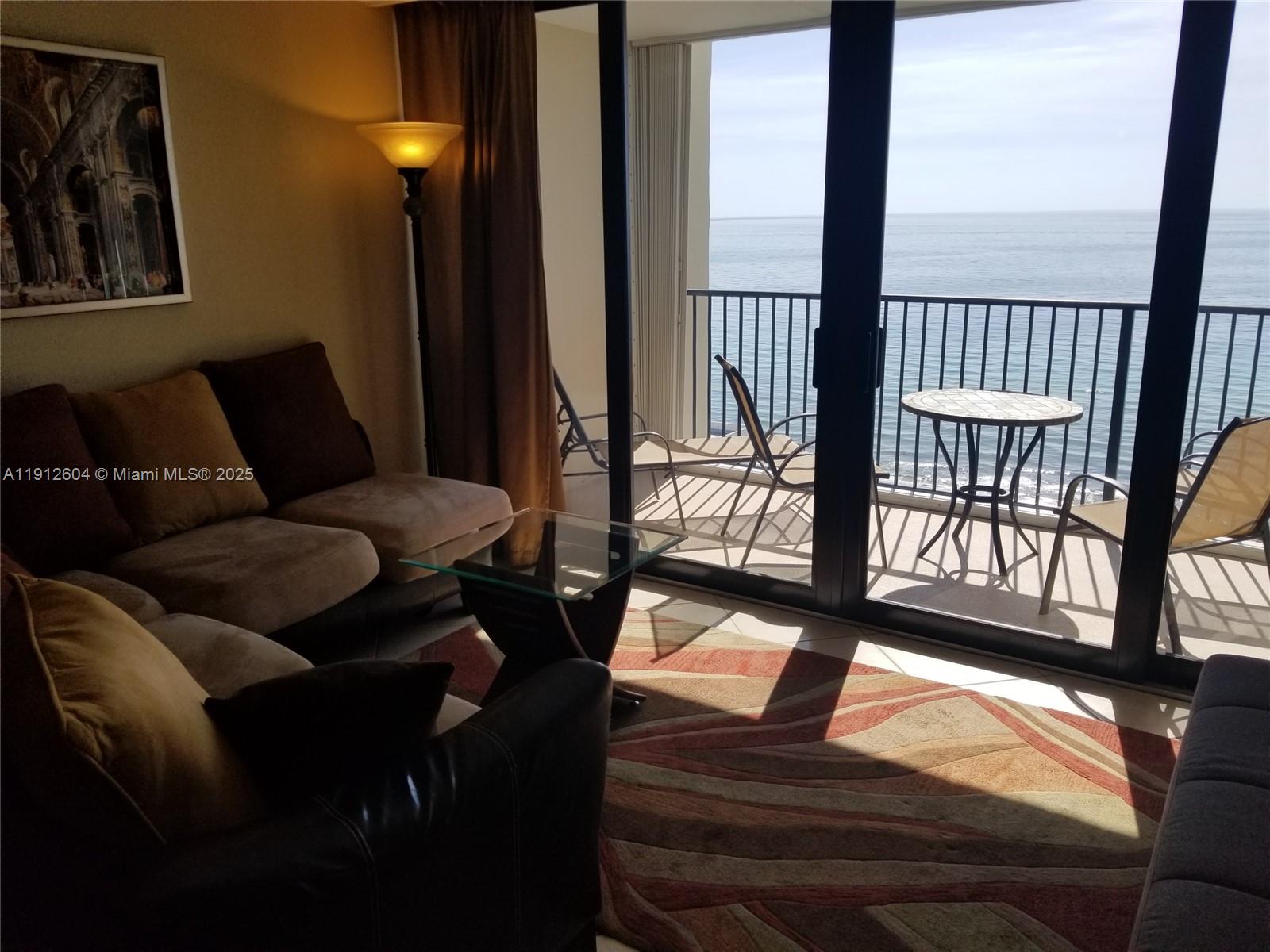 A living room with a sofa and glass table overlooks a balcony with ocean views — 2101 S Ocean Dr # 1702, Hollywood FL 33019, HOLLYWOOD, FL