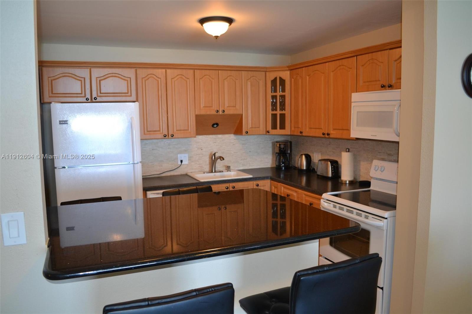 A kitchen features wood cabinets, a black countertop island, and white appliances — 2101 S Ocean Dr # 1702, Hollywood FL 33019, HOLLYWOOD, FL
