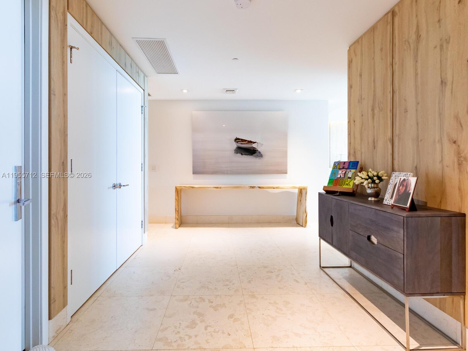 A modern hallway features light tile flooring, wood-paneled walls, a console table, and artwork — 360 Ocean Dr # 606S, Key Biscayne FL 33149, KEY BISCAYNE, FL