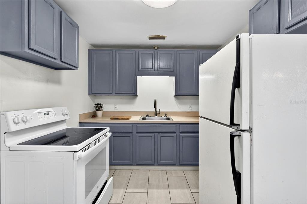 A kitchen with gray cabinets, a white refrigerator, and a wooden table in the foreground — 109 CLAIRE TERRACE, DAYTONA BEACH, FL