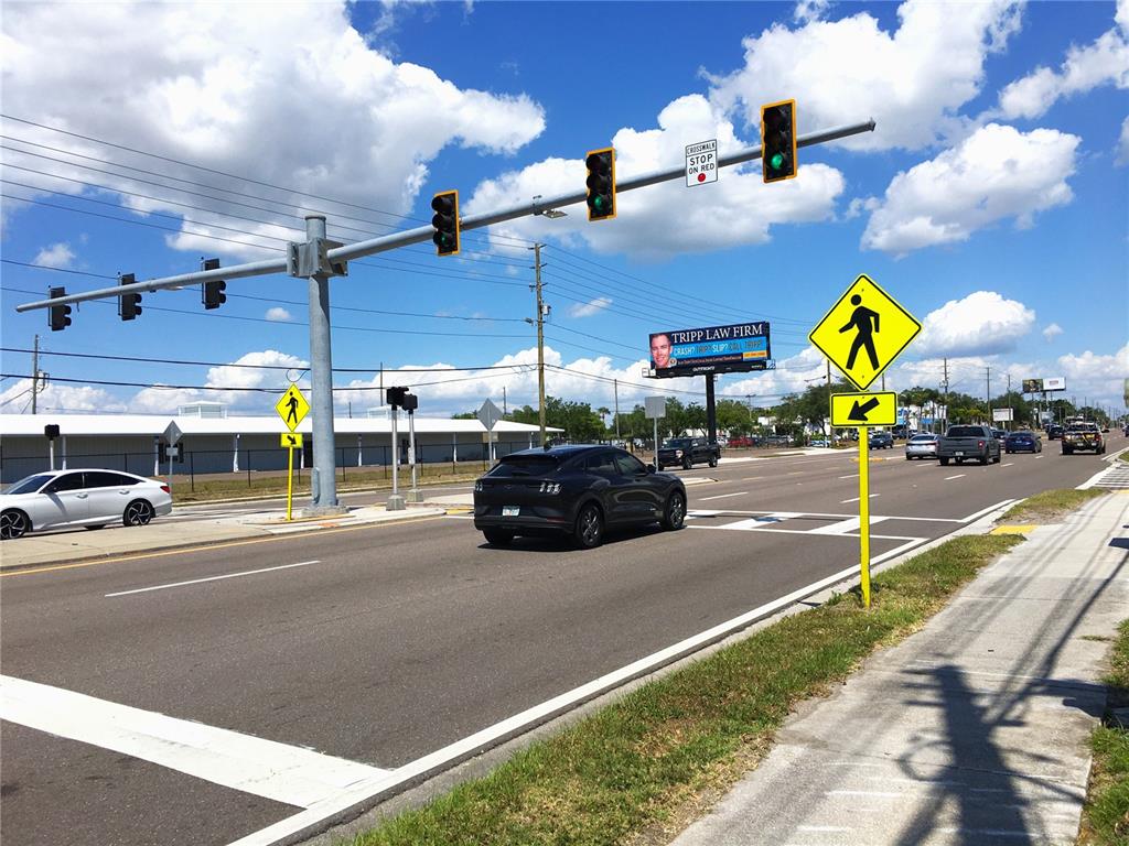 A street intersection features traffic lights, a pedestrian crossing sign, and a law firm billboard — 7900 PARK BOULEVARD N, PINELLAS PARK, FL
