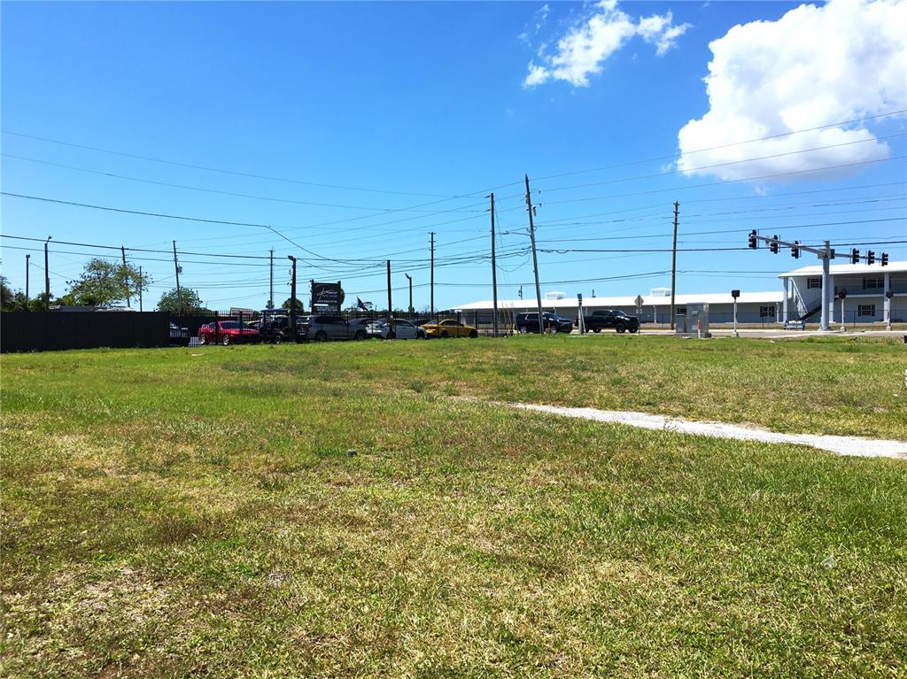 A vacant, grassy lot sits in front of a parking area with several parked cars — 7900 PARK BOULEVARD N, PINELLAS PARK, FL