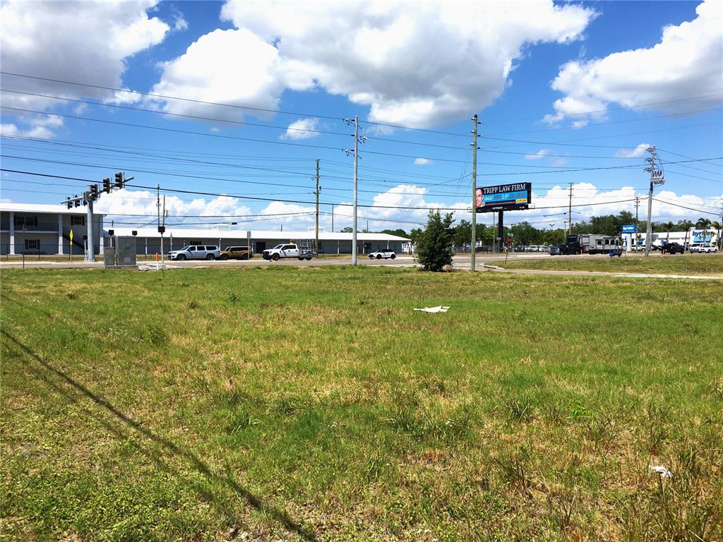 A vacant, grassy lot sits in front of a road with traffic and a billboard — 7900 PARK BOULEVARD N, PINELLAS PARK, FL