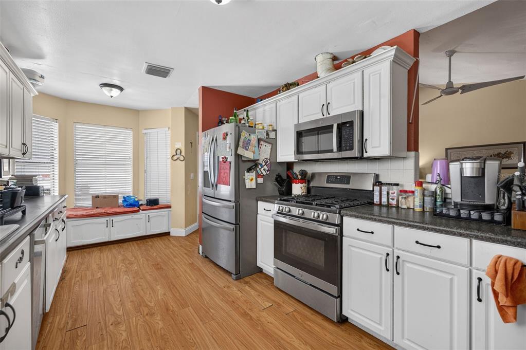 A kitchen features white cabinets, stainless steel appliances, wood-look flooring, and a window seat — 2650 ALBION AVENUE, ORLANDO, FL