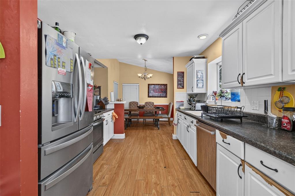 A kitchen with stainless steel appliances, white cabinets, and wood-look flooring opens to a dining area — 2650 ALBION AVENUE, ORLANDO, FL