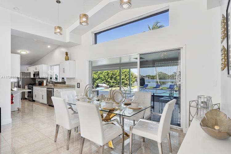 A dining area with a glass table and white chairs overlooks a pool and lake — 2541 NE 195th St # 0, Miami FL 33180, MIAMI, FL
