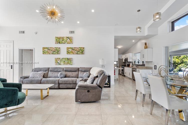 A spacious open-concept living and dining area features white tile floors and a grey sectional — 2541 NE 195th St # 0, Miami FL 33180, MIAMI, FL