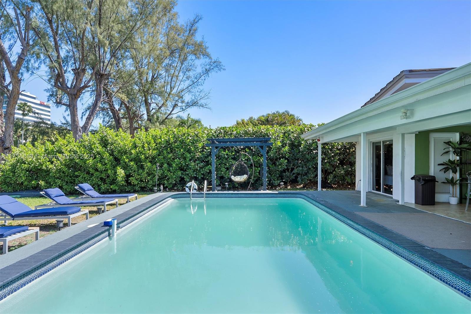 A rectangular swimming pool sits in a backyard with lounge chairs and a hanging chair — 2541 NE 195th St # 0, Miami FL 33180, MIAMI, FL
