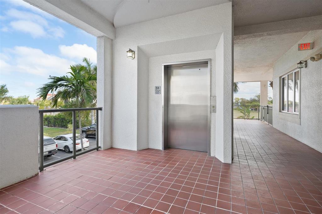 An outdoor hallway features a stainless steel elevator, tiled flooring, and a metal railing — 1030 BELLASOL WAY UNIT 3201, APOLLO BEACH, FL