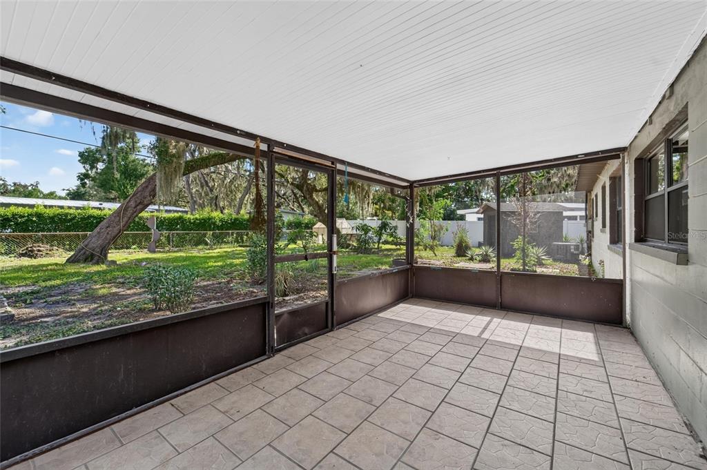 A screened-in porch with tiled flooring overlooks a grassy backyard with trees and a shed — 408 BERWICK AVENUE, TEMPLE TERRACE, FL