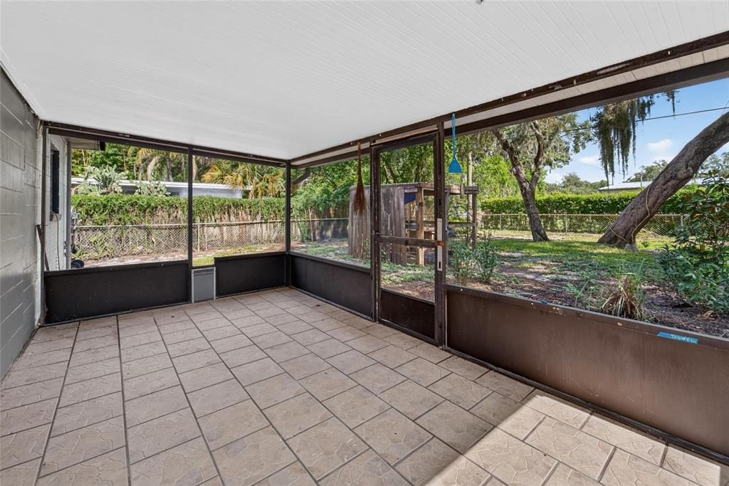 A screened-in patio with tiled flooring overlooks a backyard with trees and a wooden shed — 408 BERWICK AVENUE, TEMPLE TERRACE, FL