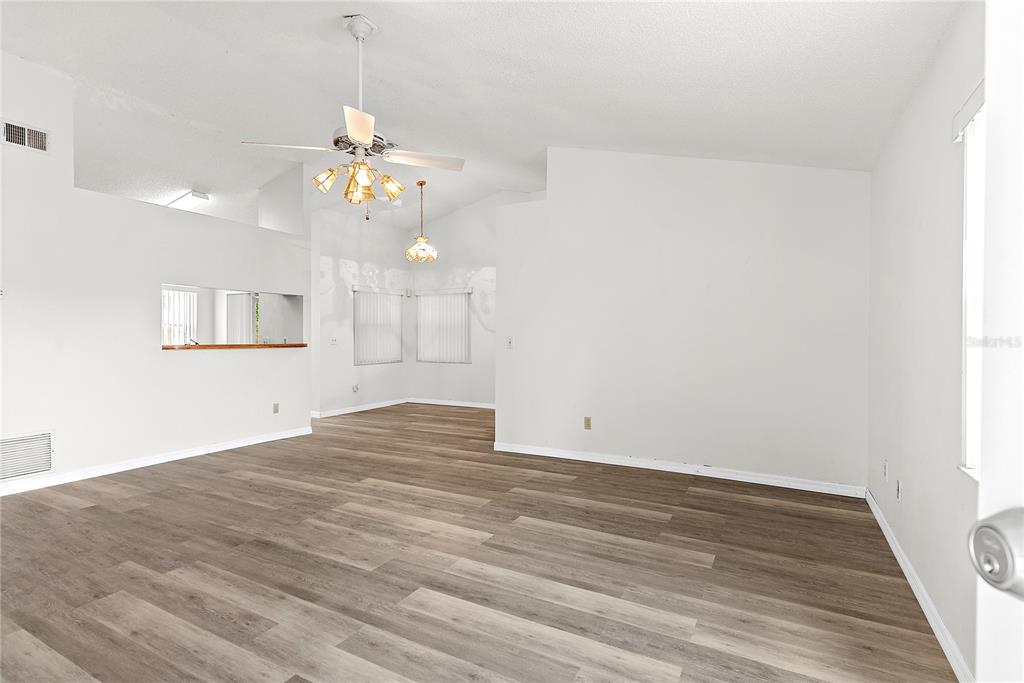An empty living room features light-colored walls, wood-look flooring, a ceiling fan, and vaulted ceilings — 49 GRAND JUNCTION BOULEVARD, ORLANDO, FL