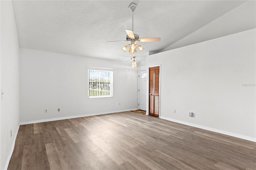 An empty living room features light wood-look flooring, white walls, a ceiling fan, and blinds — 49 GRAND JUNCTION BOULEVARD, ORLANDO, FL