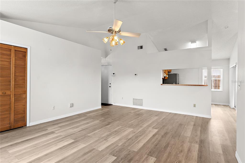 An empty living room features light wood-look flooring, a vaulted ceiling with a fan, and a pass-through window — 49 GRAND JUNCTION BOULEVARD, ORLANDO, FL
