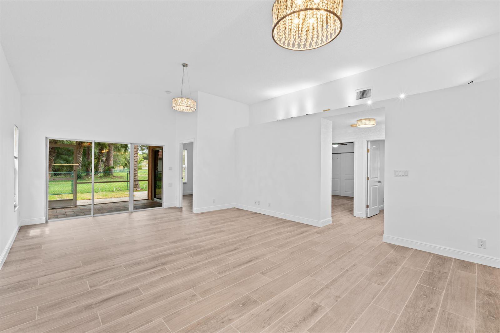 An empty living room features light wood-look tile flooring, white walls, and two drum chandeliers — 5122 Elpine Way, Riviera Beach FL 33418, RIVIERA BEACH, FL