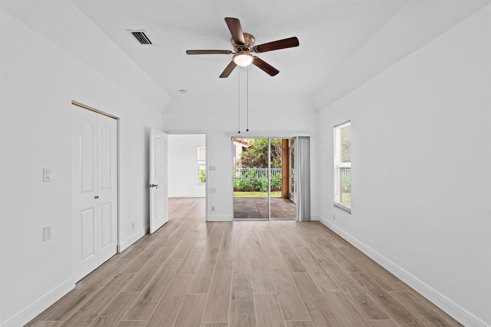 A bright bedroom features white walls, wood-look tile flooring, a ceiling fan, and sliding glass doors — 5122 Elpine Way, Riviera Beach FL 33418, RIVIERA BEACH, FL