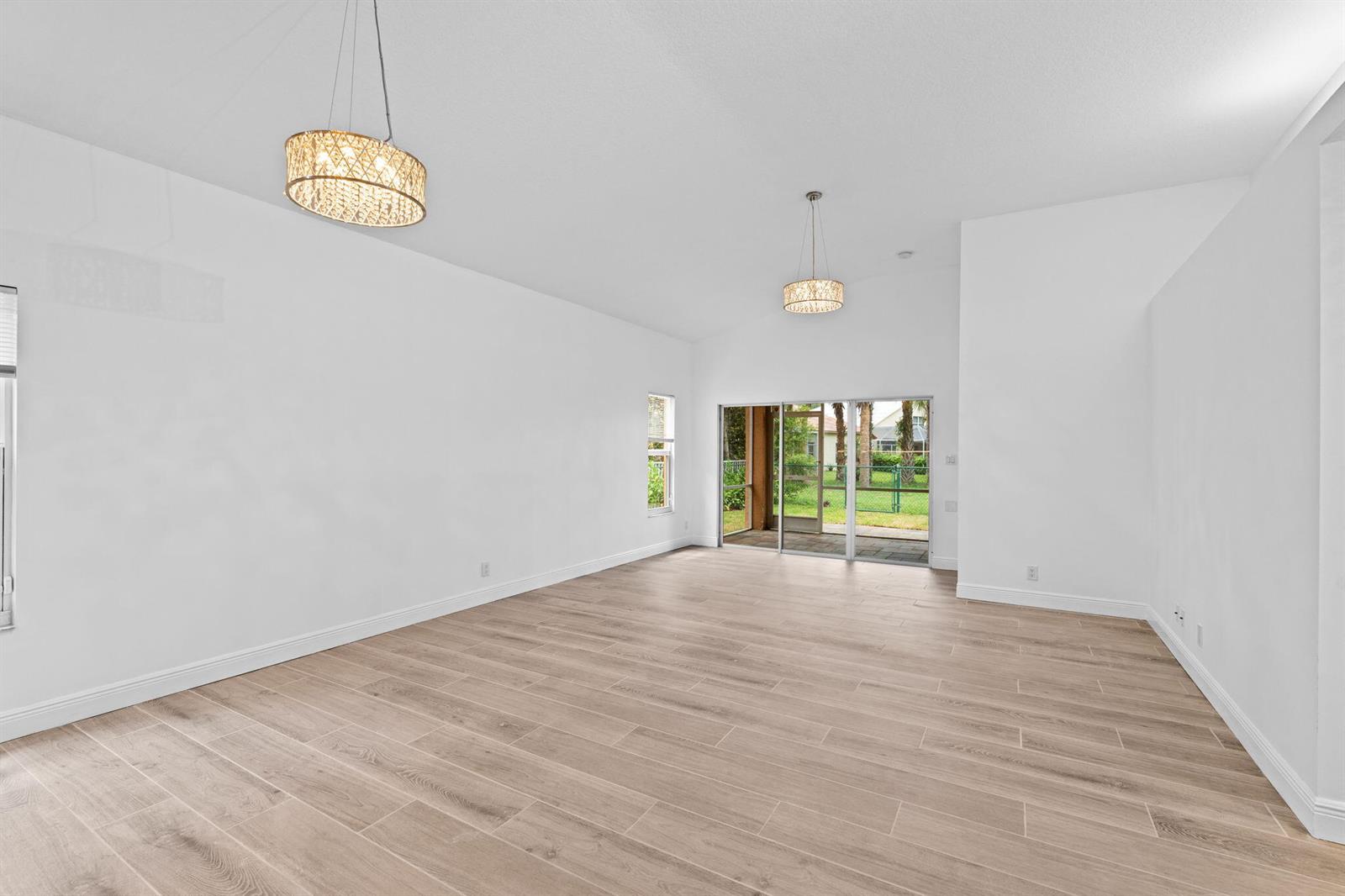 An empty living room features white walls, light wood-look tile flooring, and two pendant lights — 5122 Elpine Way, Riviera Beach FL 33418, RIVIERA BEACH, FL