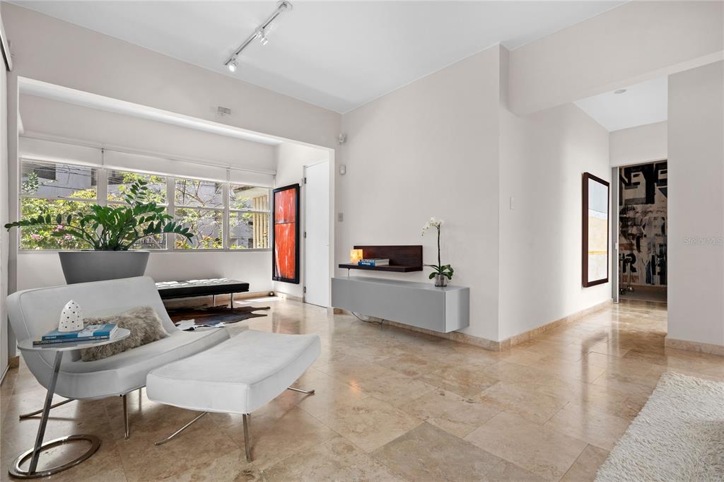 A bright living room with light tile floors, a white lounge chair, and large windows — 609 MIRAMAR AVENUE UNIT 102, SAN JUAN, PR