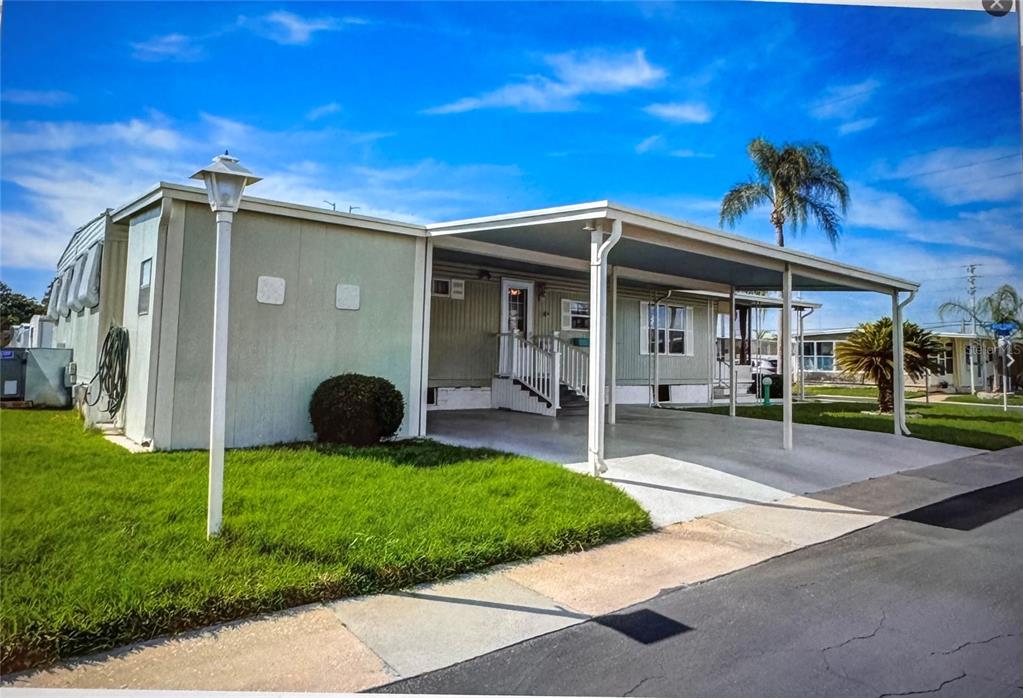 A light green mobile home features a concrete carport, white stairs, and a grassy lawn — 225 DIXIE LANE, TARPON SPRINGS, FL