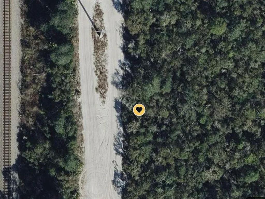 This aerial view shows a dirt path running alongside a railroad track and dense forest — 0 RIEGEL (PAPER) AVENUE, ORANGE CITY, FL