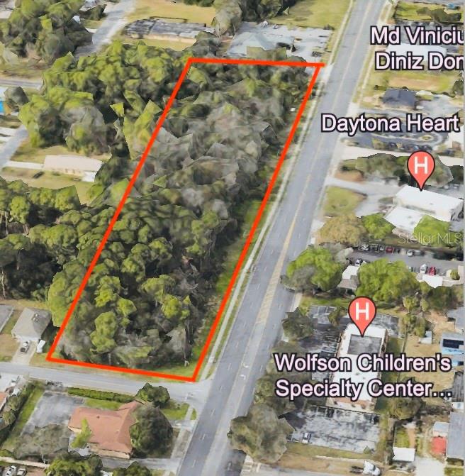 An aerial view shows a rectangular, tree-covered vacant lot outlined in red next to a road — 650-700 N CLYDE MORRIS BOULEVARD, DAYTONA BEACH, FL