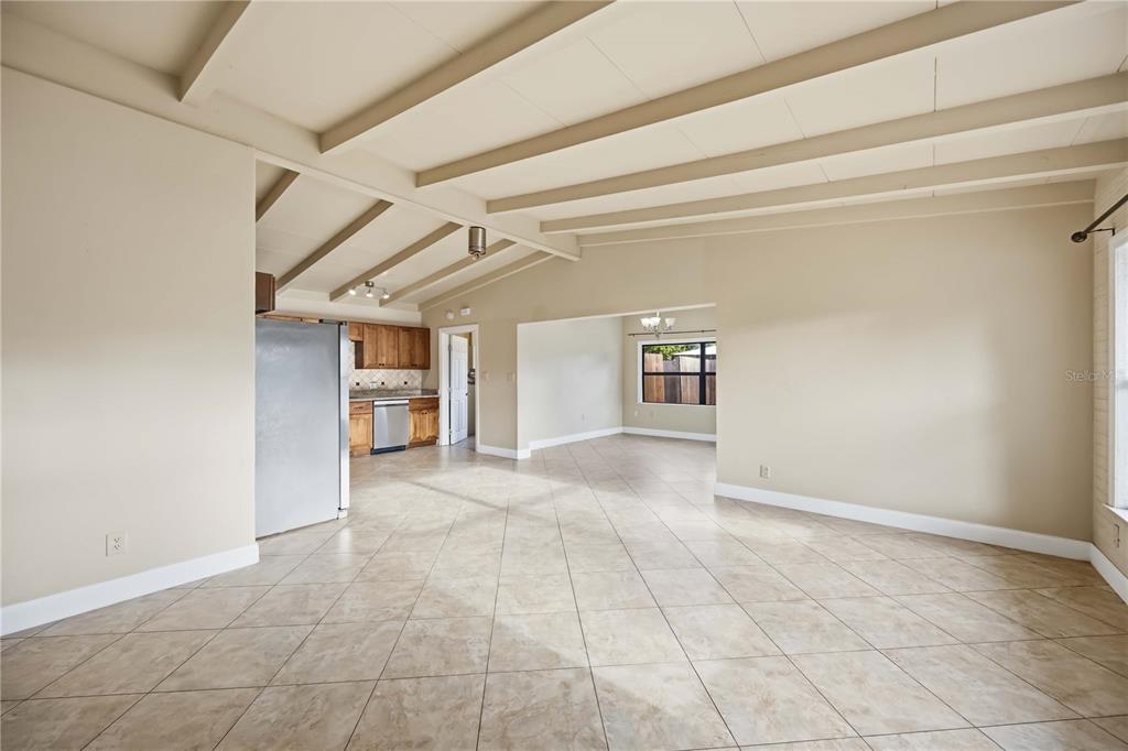 An open-concept living area with tile floors, exposed ceiling beams, and an adjacent kitchen — 2715 INGOT PLACE, SARASOTA, FL