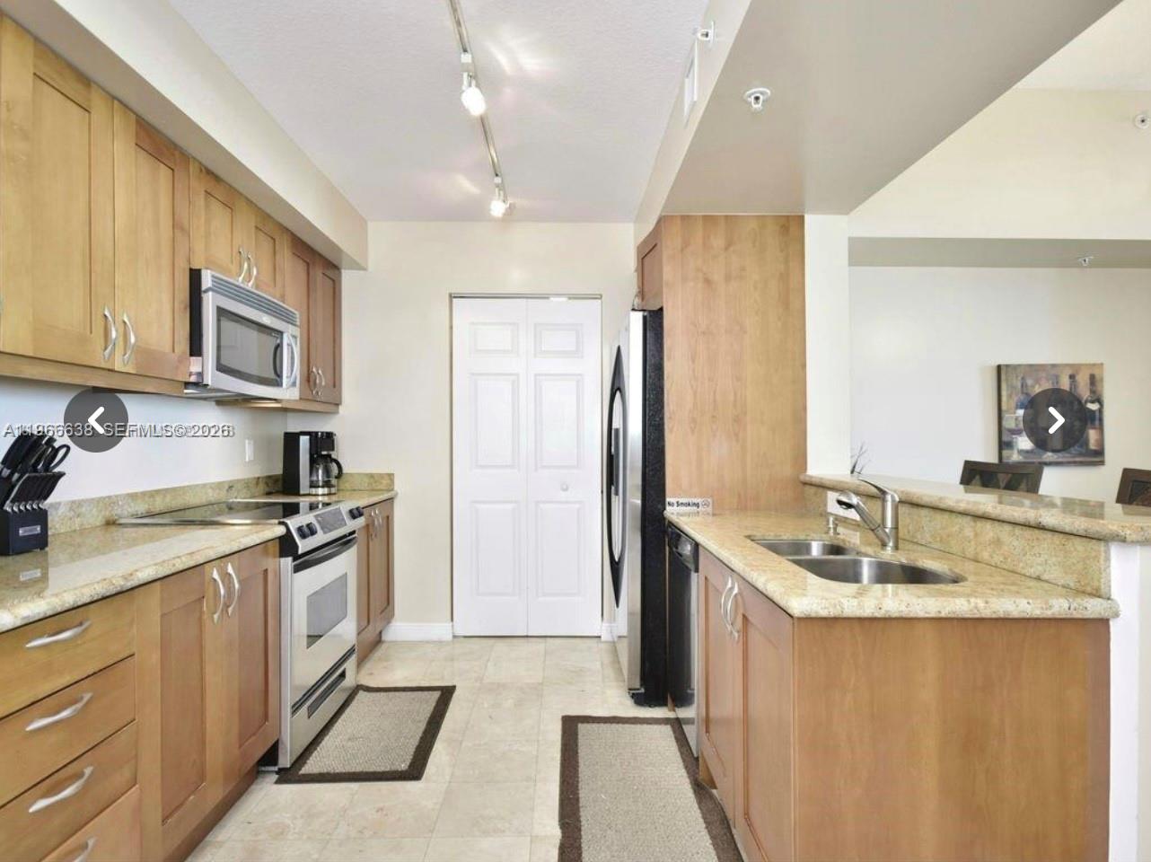A galley kitchen features light wood cabinets, granite countertops, and stainless steel appliances — 1755 E Hallandale Beach Blvd # 2505E, Hallandale Beach FL 33009, HALLANDALE BEACH, FL