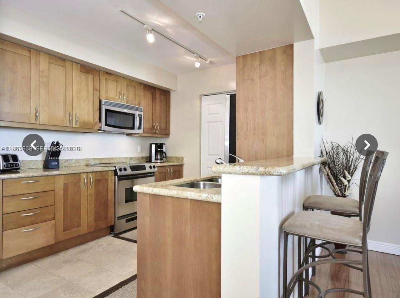 A kitchen with light wood cabinets, granite countertops, and a breakfast bar with two stools — 1755 E Hallandale Beach Blvd # 2505E, Hallandale Beach FL 33009, HALLANDALE BEACH, FL