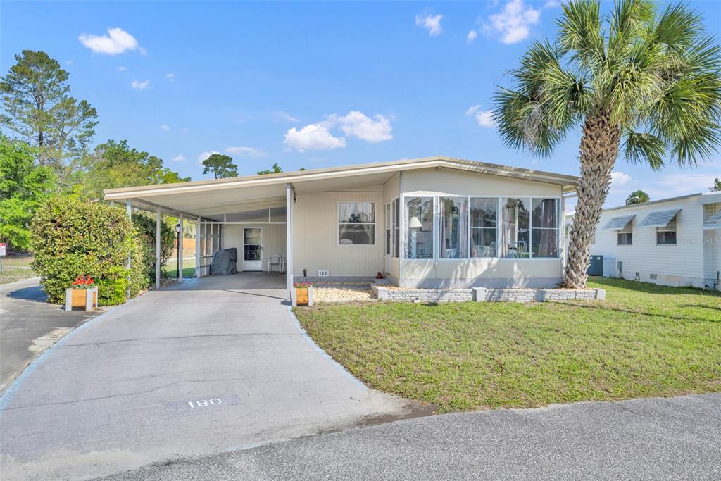 A single-story manufactured home features a carport, a screened-in porch, and a palm tree — 180 PARADISE N, LEESBURG, FL