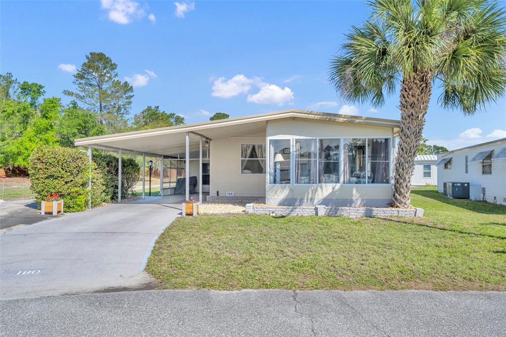 A single-story manufactured home features a carport, a sunroom, and a palm tree in front — 180 PARADISE N, LEESBURG, FL